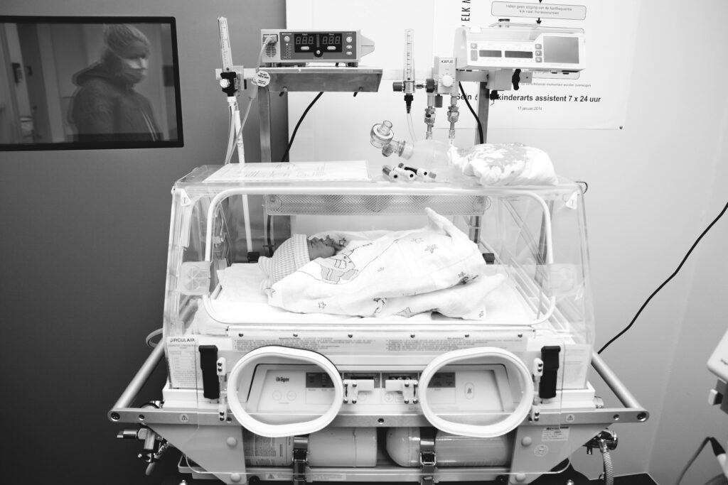 Black and white image of newborn in a softly lit hospital incubator, representing hope and resilience.